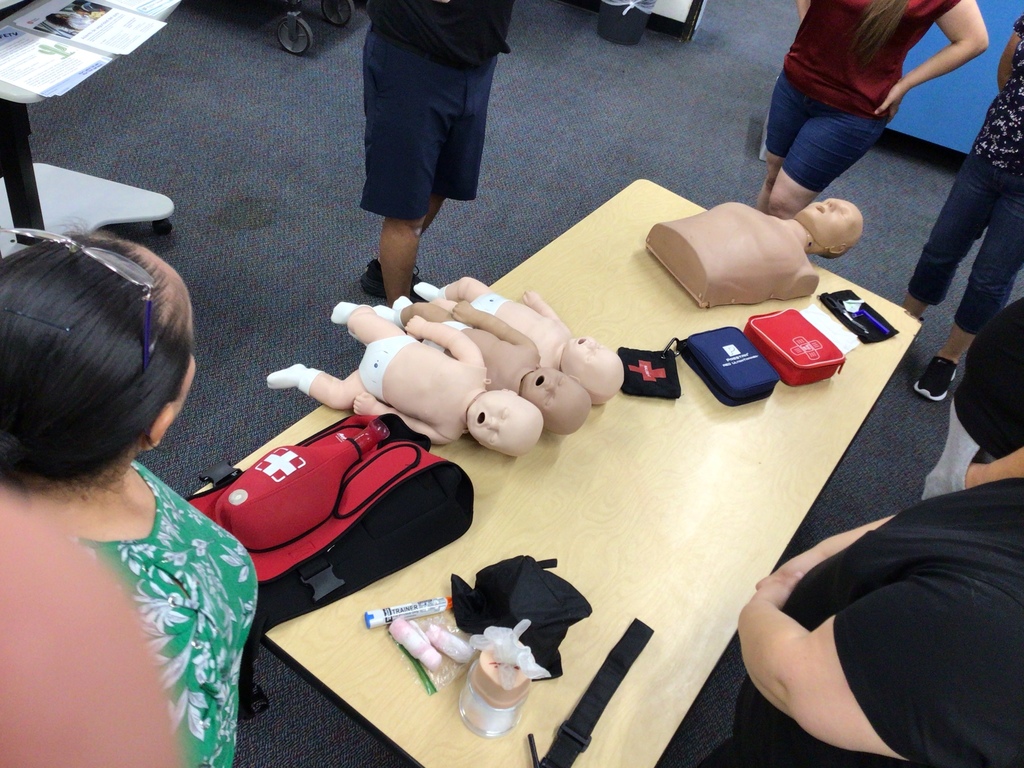 First Aid, Defibrillator, Narcan kits with baby mannequins on table.