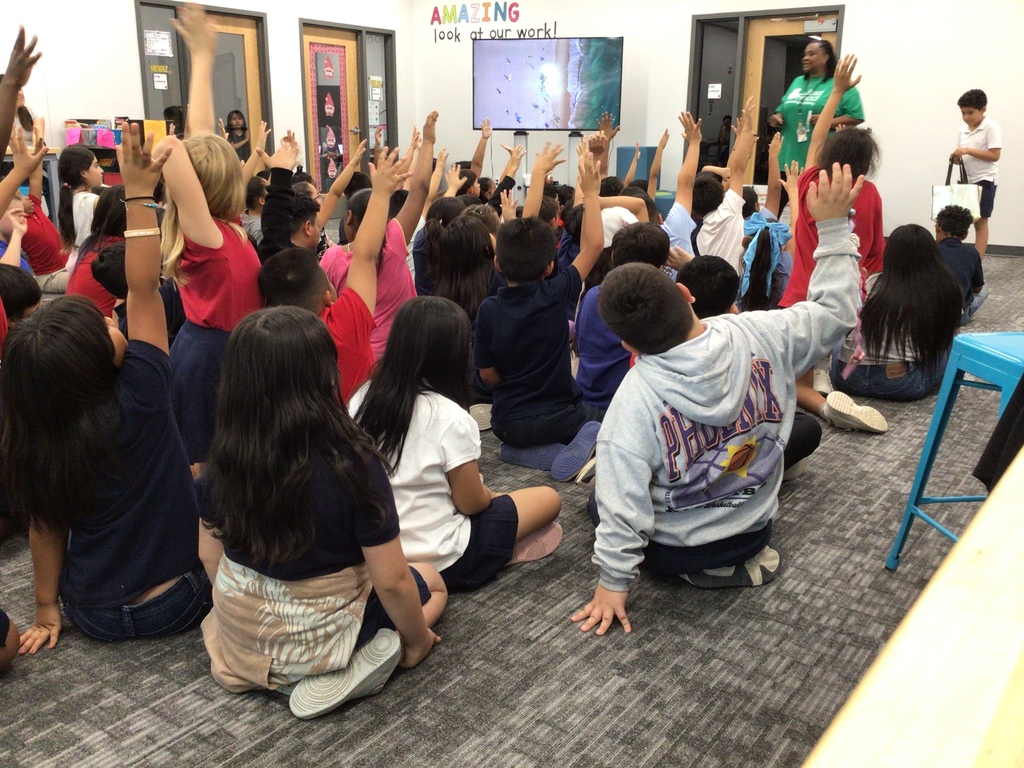 Students sitting on floor raising their hands.