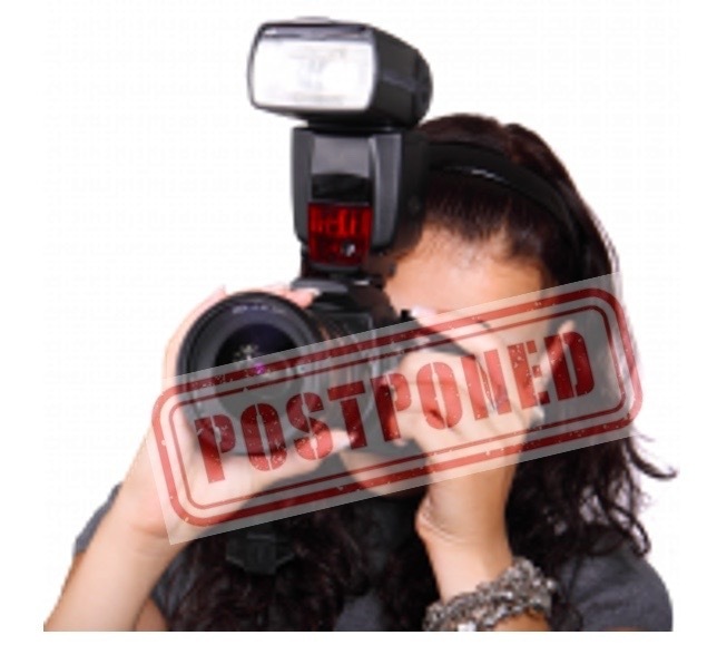 woman holding black digital camera with big lens. Red postponed sign in front