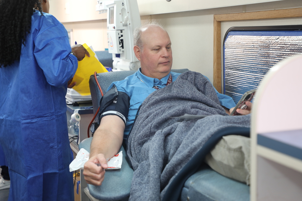 An older man reclines on a hospital bed while a healthcare worker prepares to take his blood.