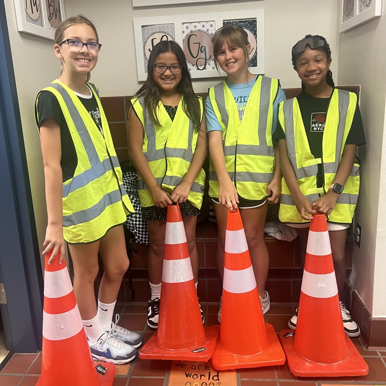 four girls wearing yellow safety vests and holding red cones