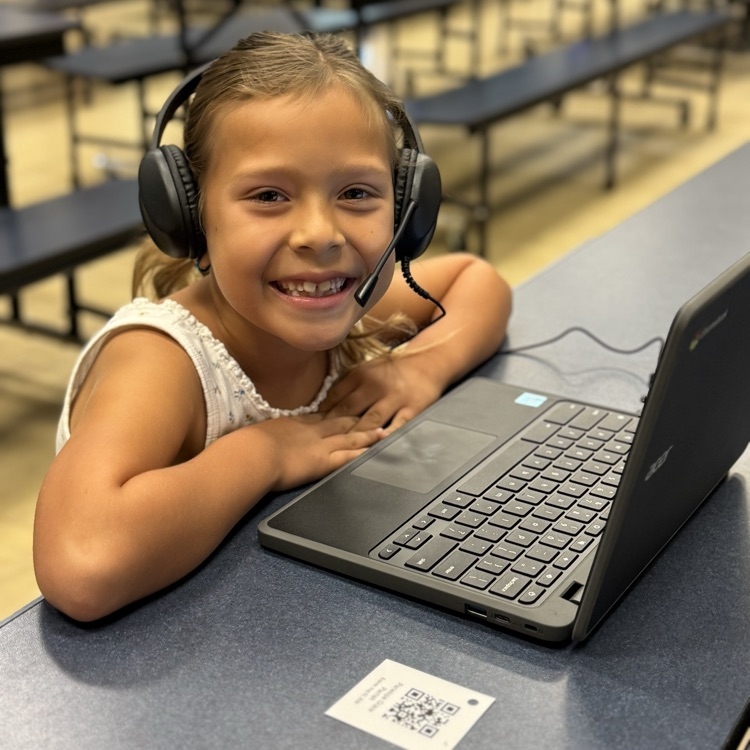 little girl sitting at computer with headphones on smiling