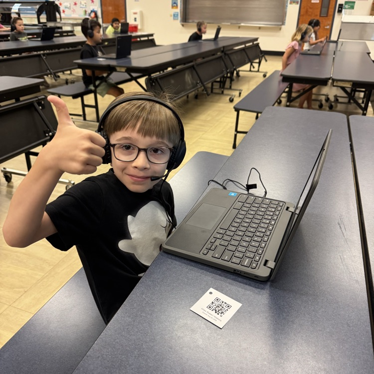 boy sitting at computer with headphones on giving thumbs up