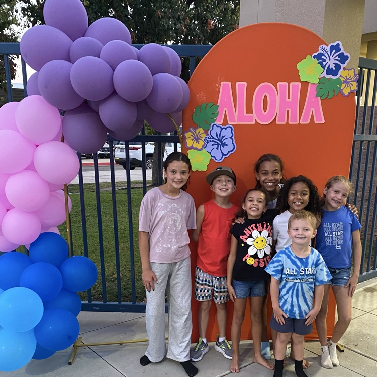 group of kids smiling standing in front of Aloha sign and ballons