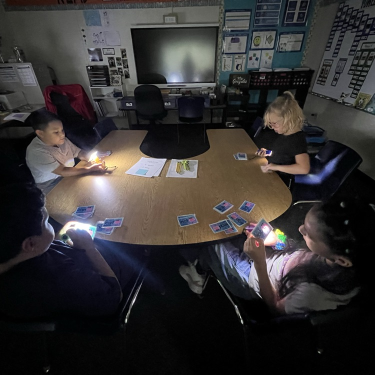 students sitting at table with flashlights 
