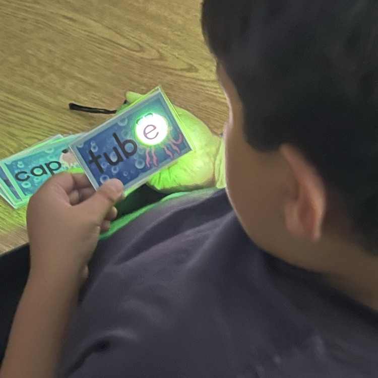 boy looking at a flashcard with a flashlight shining through the back of it