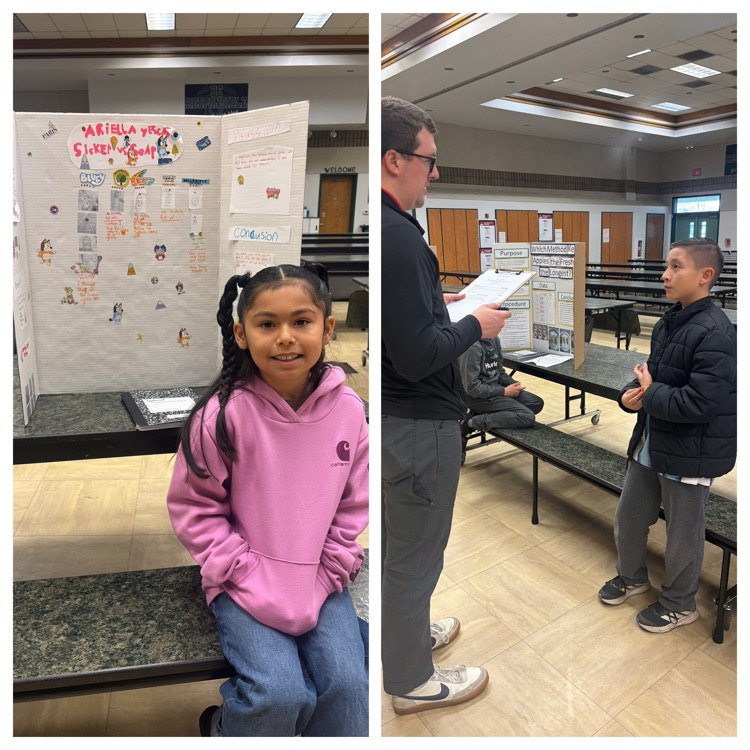 girl sitting in front of science fair project and a man talking to a boy