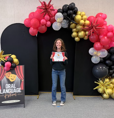 student with certificates in front of balloons 