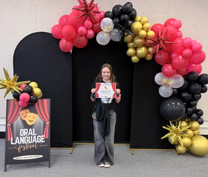 student with certificates in front of balloons 