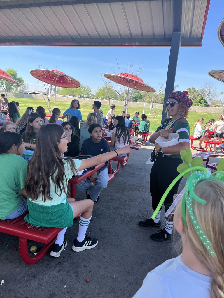 students sitting a red tables with adult dressed as a leprechaun.