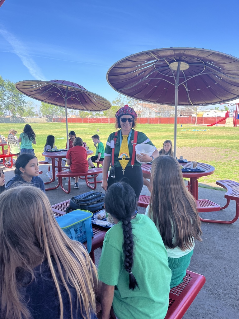 students sitting a red tables with adult dressed as a leprechaun.