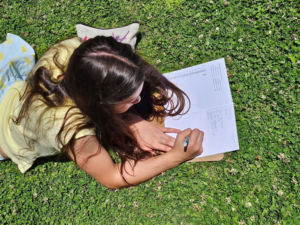 student writing in journal on grass