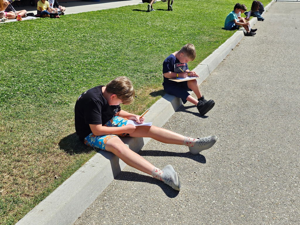 students writing in journal sitting on a curb