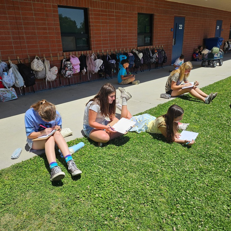four girls sitting outside writing