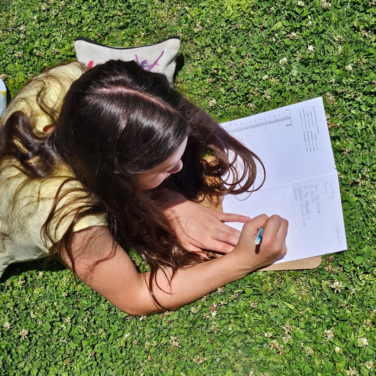 girl laying on her stomach working on a writing assignment 