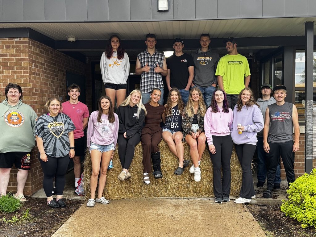senior prank crew sitting on large straw bale in front of High school office.