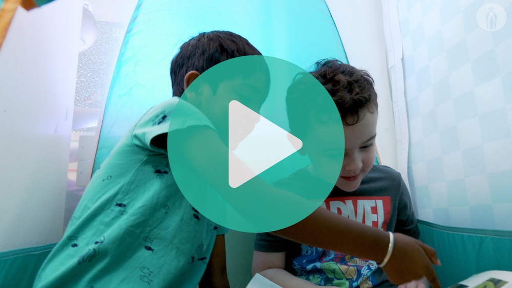 Two pre-k students sitting in a tent reading a book together.