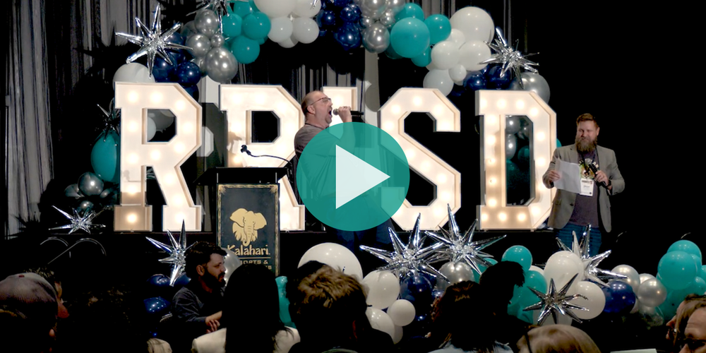 Stage with man yelling into microphone and big letters that say R R I S D 