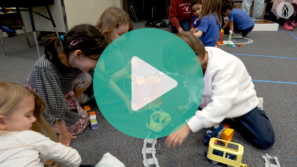 Students sitting on the floor playing with a robotic train set