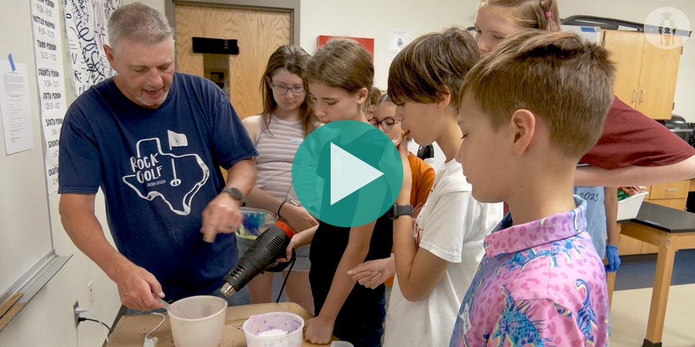 Picture of teacher stirring hot wax to make candles while students observe and learn
