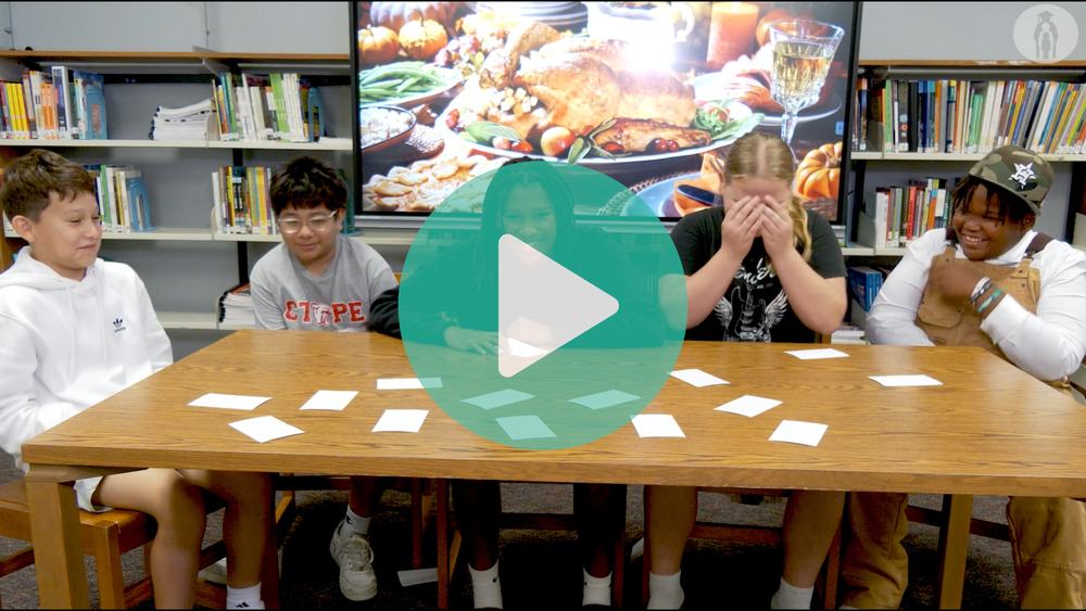 Image of middle school students sitting around a table telling jokes and luaghing.