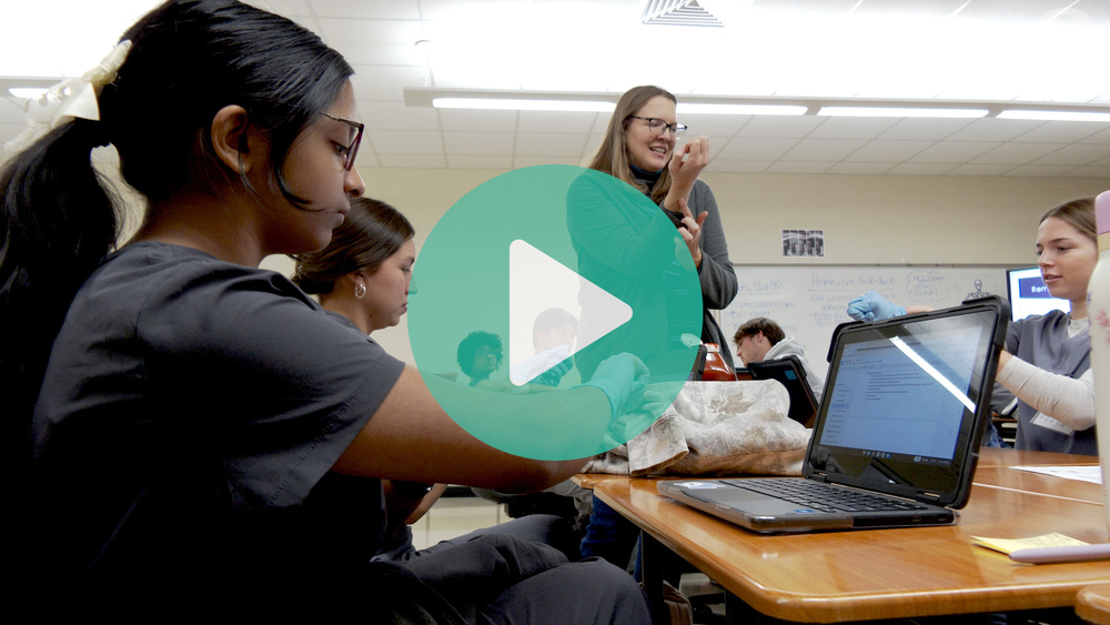 Picture of teacher standing in front of students showing them how to remove gloves.