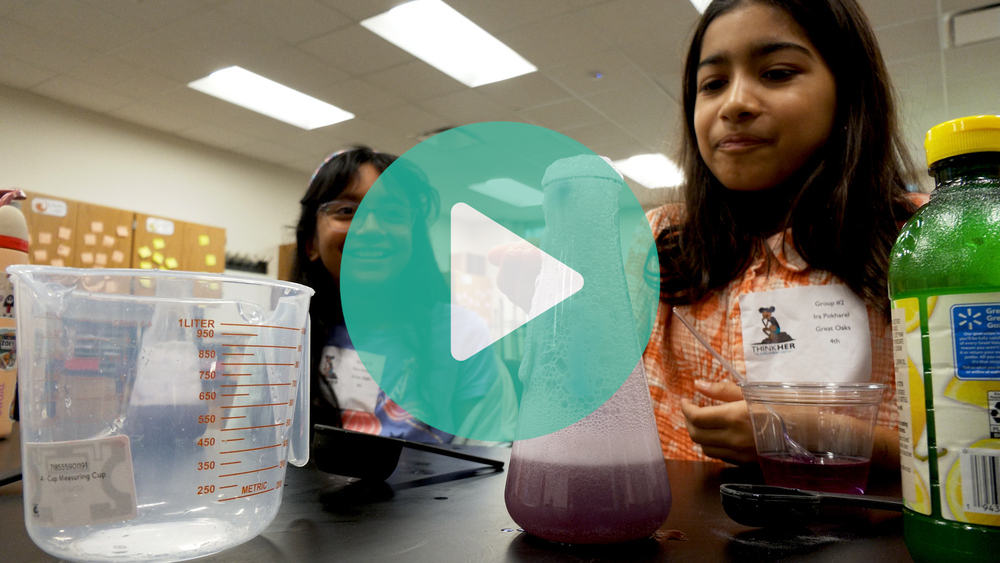 Picture of a girl in a lab looking at a beaker that is overflowing with foamy liquid