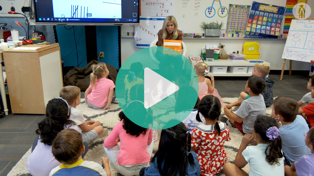 Kindergarten teacher sitting in front of class reading a book.