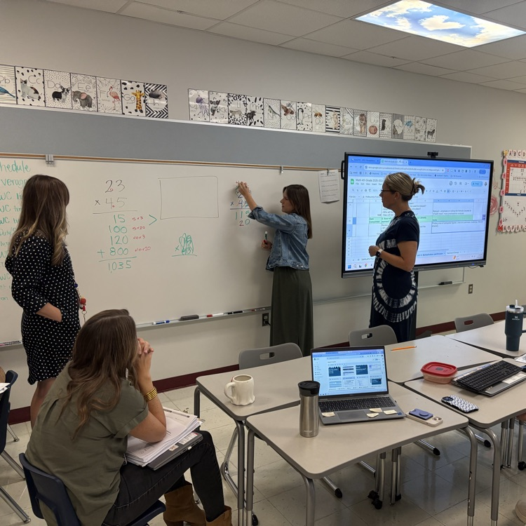 4th grade teachers collaborate on instructional strategies for teaching multiplication, working at a whiteboard in a classroom.