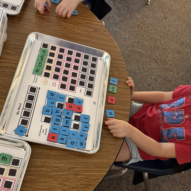 Close up of a student using a magnetic tray with a phonetic word building system, featuring individual letter tiles for consonants, vowels, and consonant digraphs.