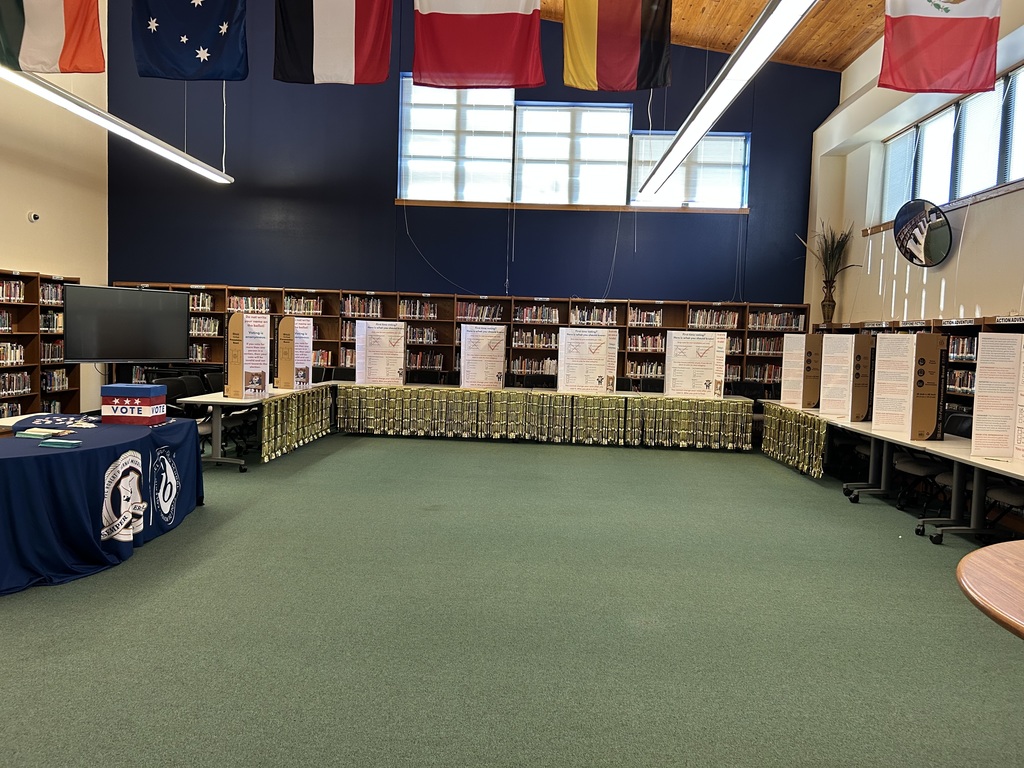 Voting booths and the table with a ballot box that says 'Vote' and the Hernandez and IB logo on a blue tablecloth.
