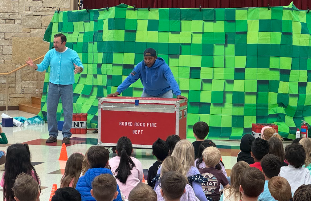 Two People standing in front of green back drop and behind a big red case