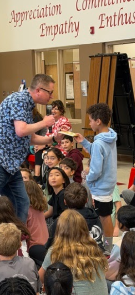 Author John Schu standing in front of children handing book to student