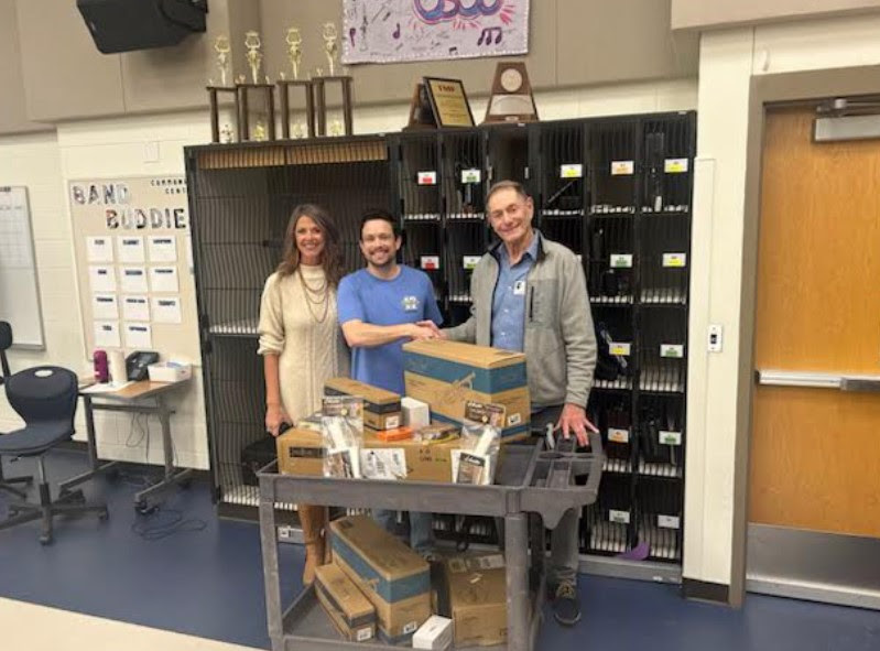 Mr. Pedersen shaking hands and accepting new instruments for his program standing with Ms. Winnek and a donor. 