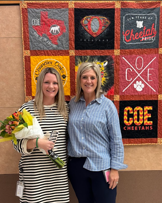 Photo of Teacher of the Year and Principal holding flowers, standing in front of a quilt