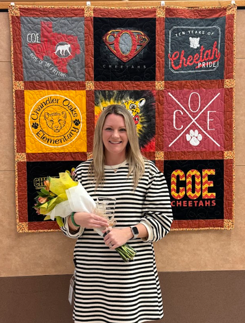 Photo of Teacher of the Year holding flowers standing in front of a quilt
