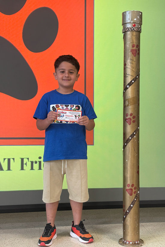 Student standing in front of orange and yellow screen, holding a certificate, standing next to the impossible shot tube