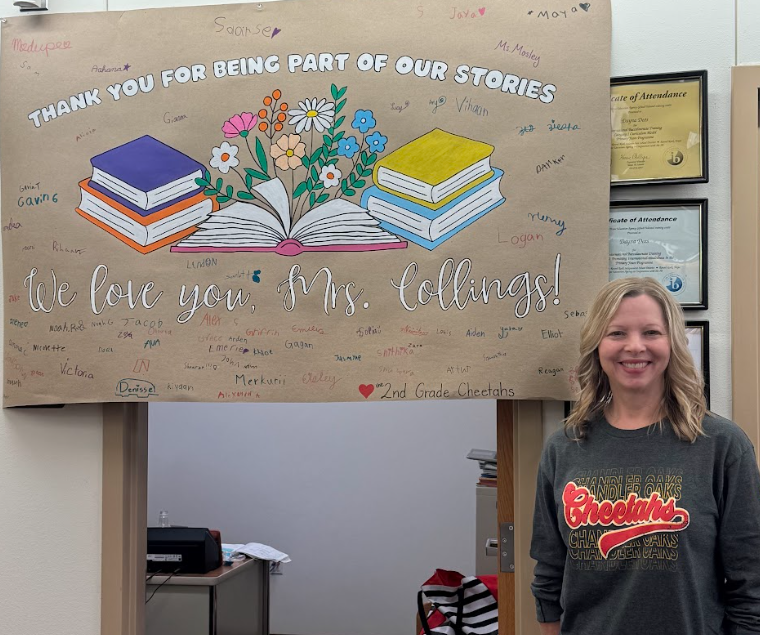 Photograph of our librarian Mrs. Collings standing in front of sign with books and flowers that says "Thank you for being part of our stories We love you Mrs. Colings!"