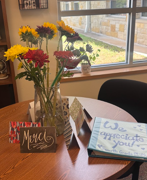 Photograph of yellow and red flowers in vase on table with thank you cards and a binder that says We appreciate you! Fourth Grade