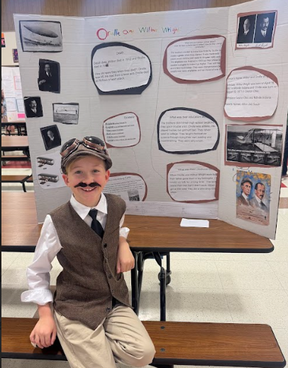 Photograph of student standing in front of table with trifold board on it