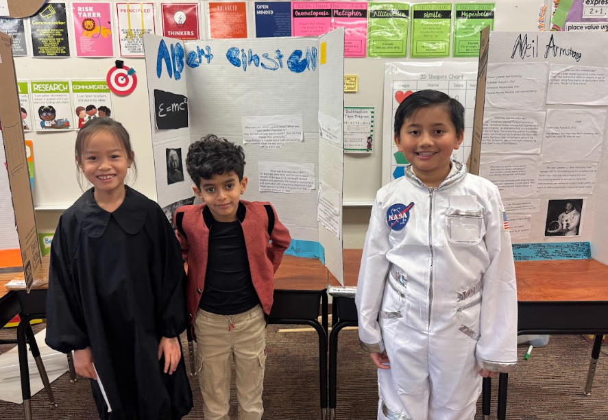 Photograph of three students standing in front of desks with trifold boards on them