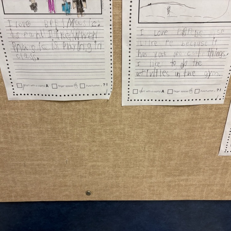 A close-up of student writing samples on a bulletin board, sharing their love for music and PE classes.