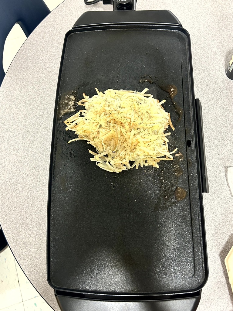 A pile of seasoned, shredded potatoes cooking on an electric griddle.