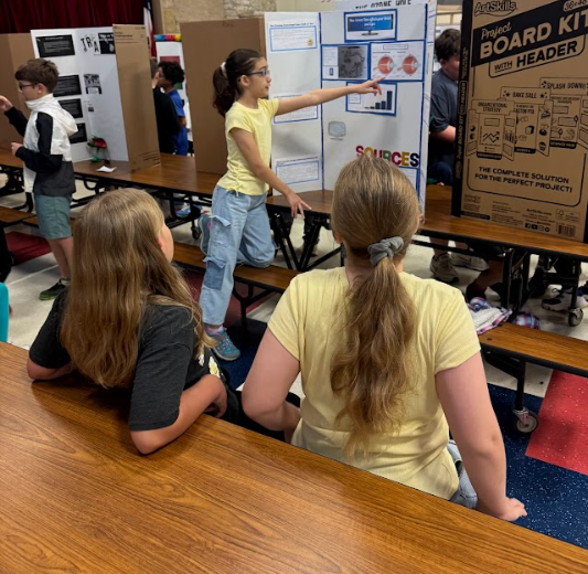 Two students standing listening to another student speak in front of trifold 