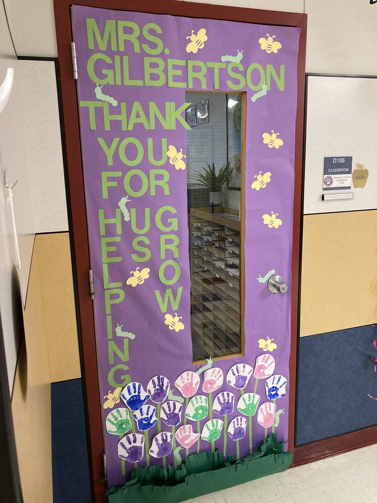 A classroom door is decorated with purple paper, green lettering that reads Thank You For Helping Us Grow, and paper flowers made from colorful student handprints.