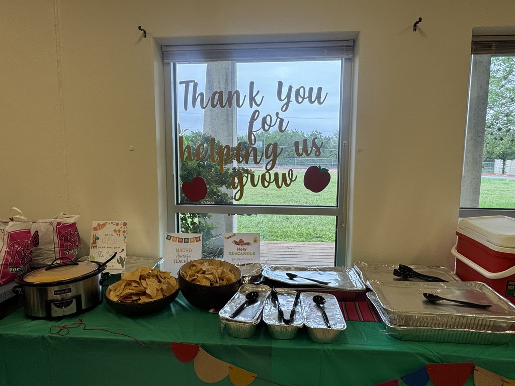 Chips, questo, and containters of food sitting on table with green tablecloth in front of window with sign that says "Thank you for helping us grow"