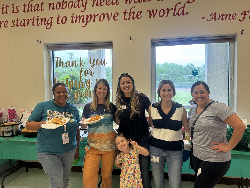 Two teachers and 3 PTA members and 1 child standing in front of table with green table cloth, in front of two windows. Sign saying "Thank you for helping us grow" sign
