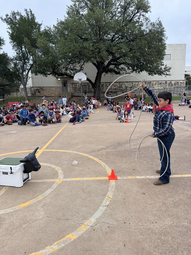 4th grade boy dressed up as a cowboy and trying to lasso a fake cow.