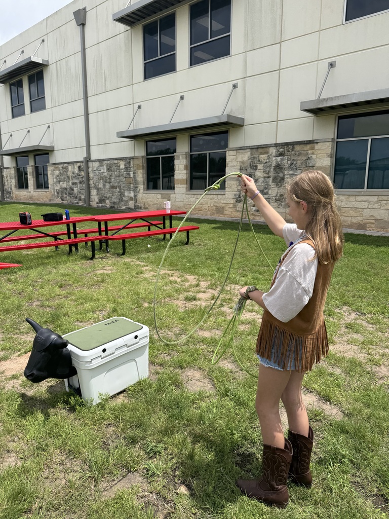 A girl dressed as a cowgirl and lassoing a fake cow.