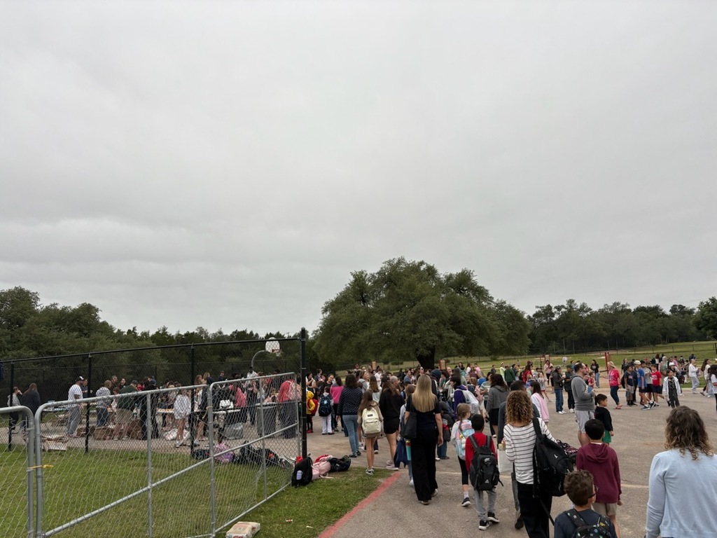 A large crowd of parents and elementary students gather on an outdoor school blacktop and playground area for a morning event.